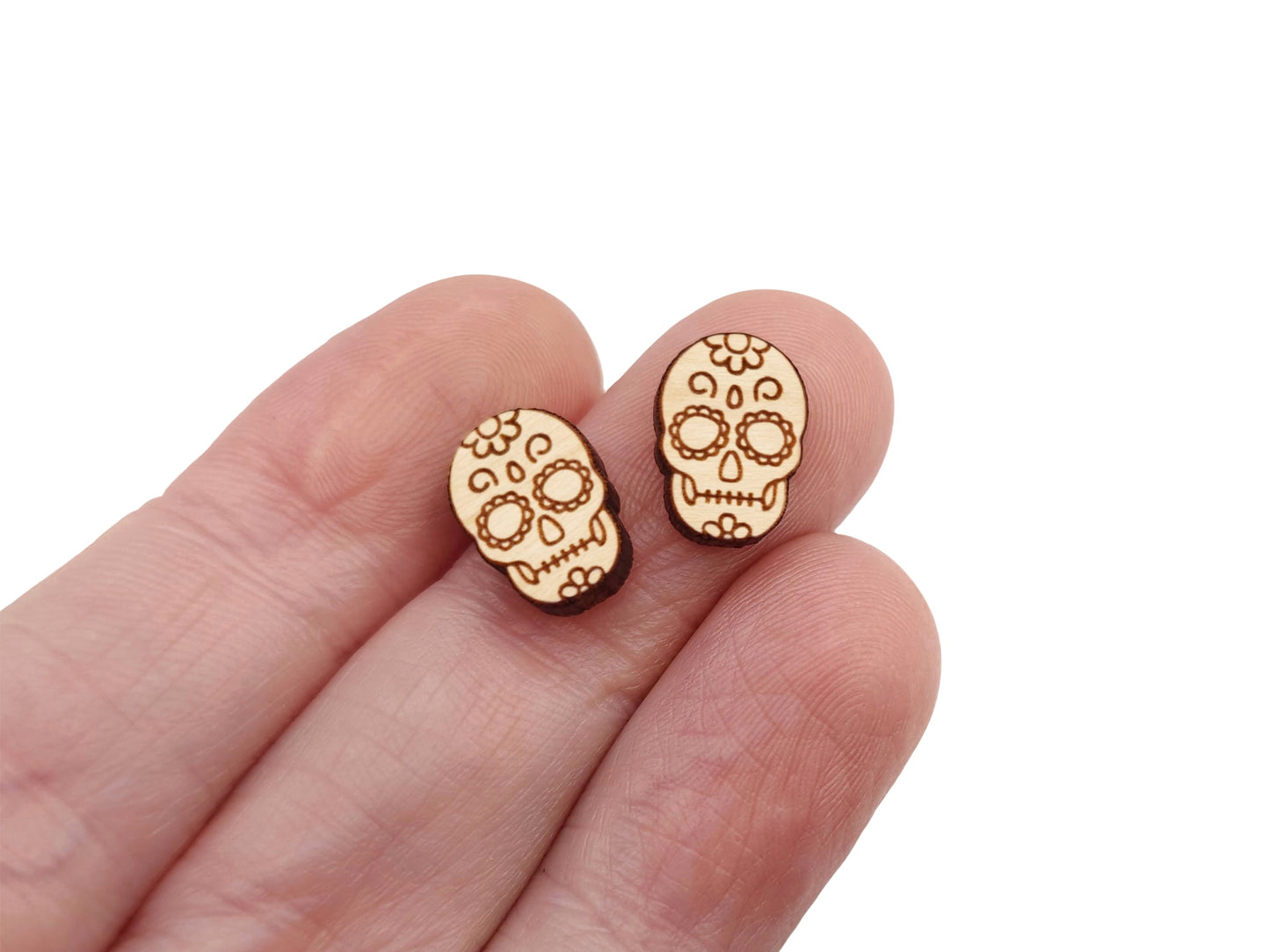 a hand holding a pair of wooden cabochon stud earring blanks cut and engraved to look like a sugar skull