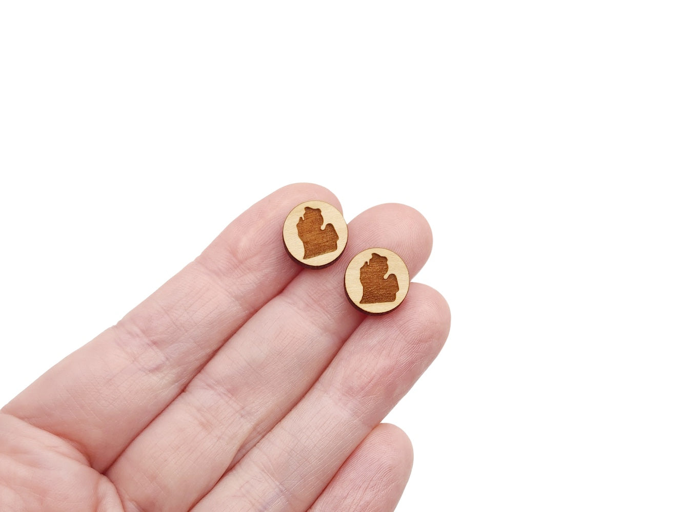 a hand holding a pair of round wooden cabochon earring blanks engraved with the Michigan mitten