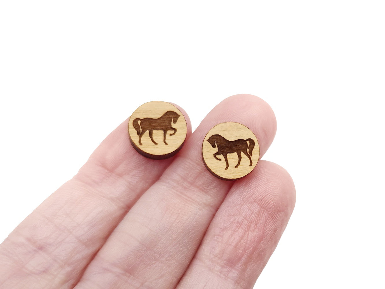 a hand holding a pair of earrings with a horse on it