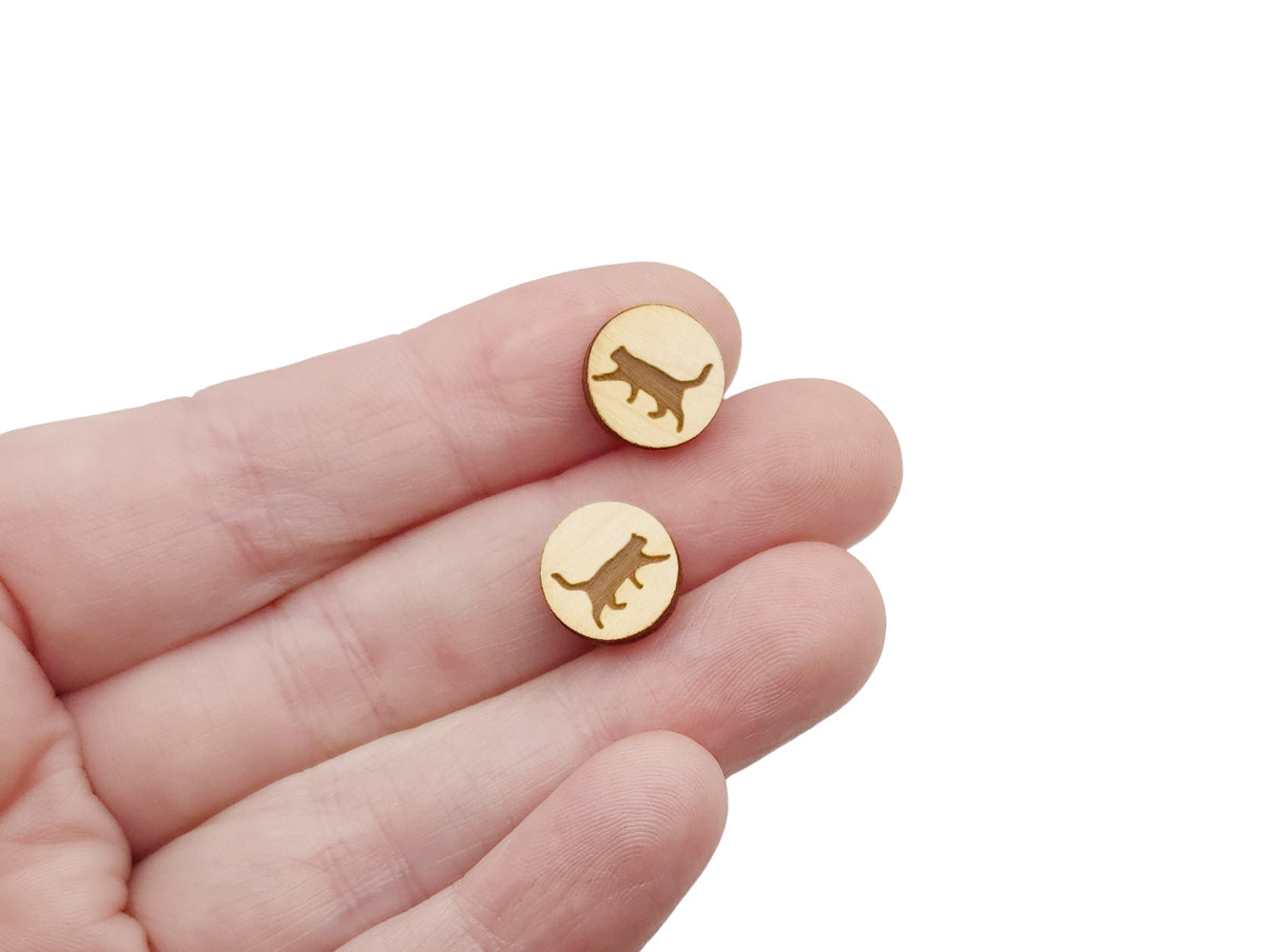 a hand holding a pair of round wooden cabochon earring blanks engraved with a cat silhouette