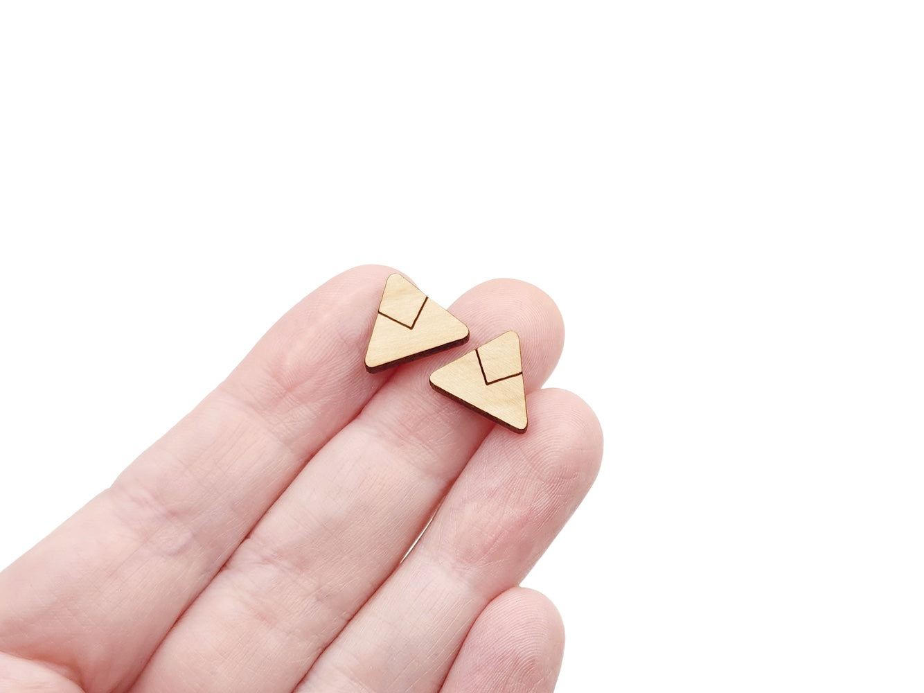 a hand holding a pair of wooden cabochon stud earring blanks cut and engraved to look like a triangle with a chevron line