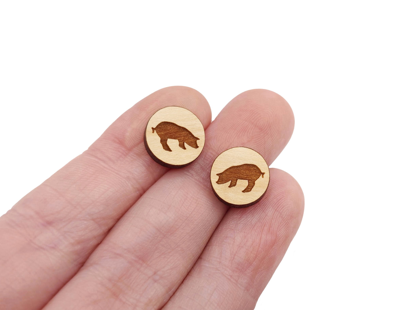 a hand holding a pair of round wooden cabochon earring blanks engraved with a pig silhouette