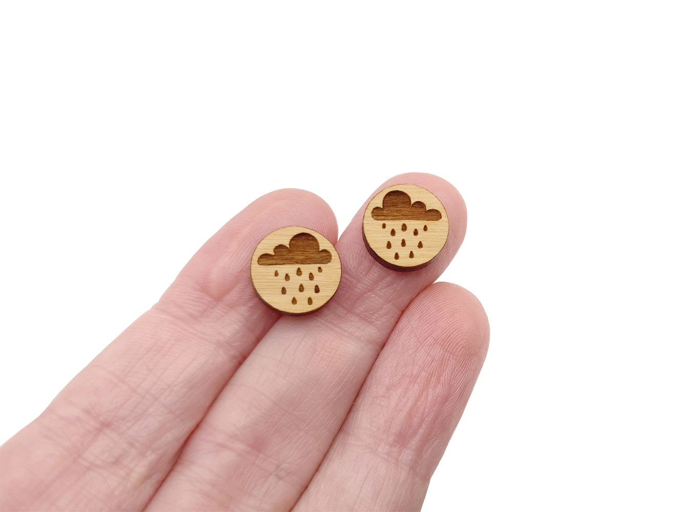 a hand holding a pair of round wooden cabochon earring blanks engraved with a rain cloud design