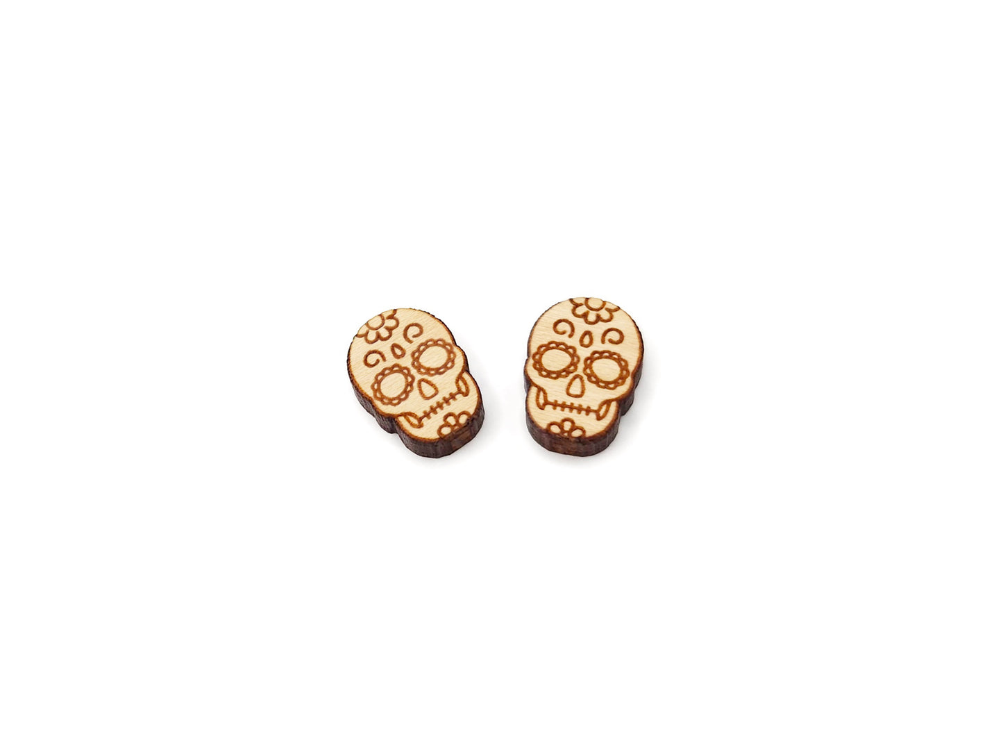 a pair of wooden cabochon stud earring blanks cut and engraved to look like a sugar skull