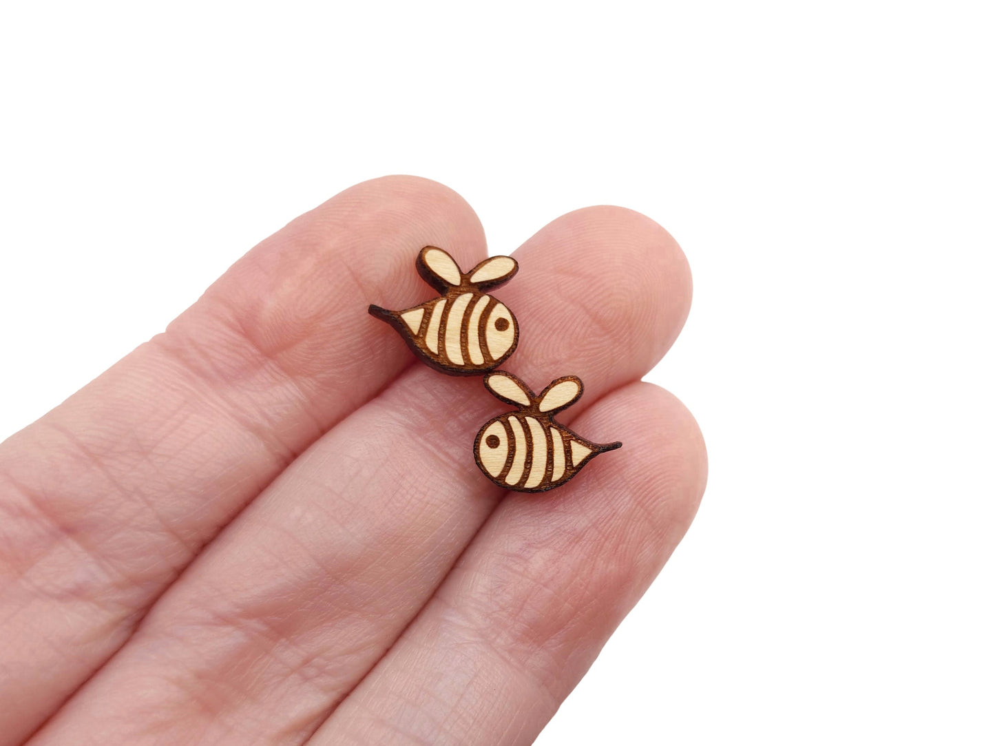 a hand holding a pair of round wooden cabochon earring blanks cut and engraved to look like a bee