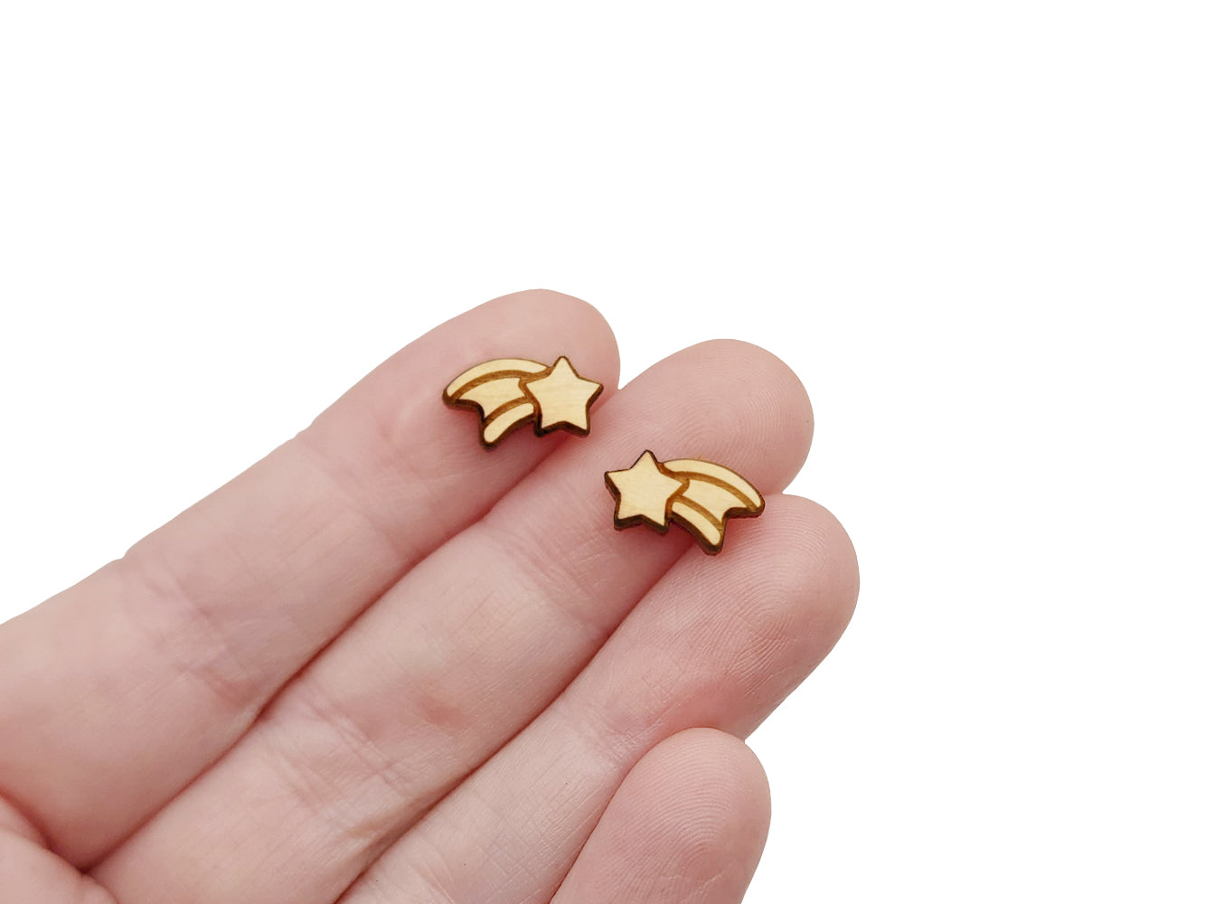 a hand holding a pair of wooden cabochon stud earring blanks cut and engraved to look like a shooting star