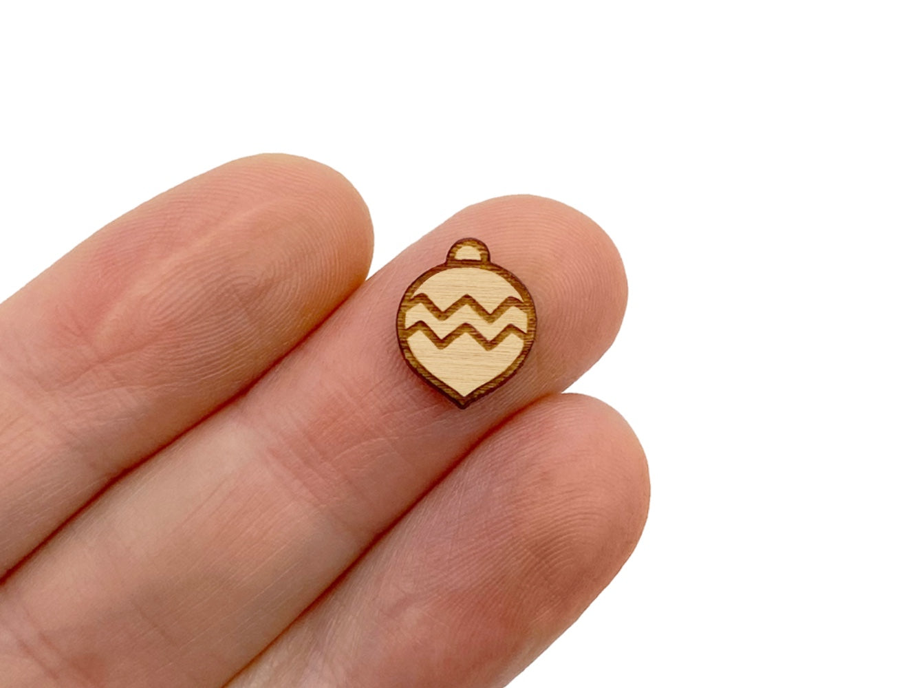 a hand holding a wood cabochon stud earring blanks cut and engraved to look like a Christmas ornament