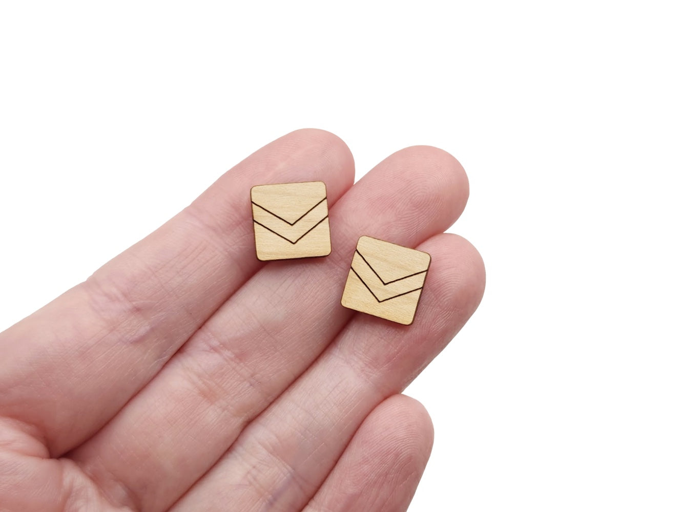 a hand holding a pair of wooden cabochon stud earring blanks cut in a square shape and engraved with a chevron