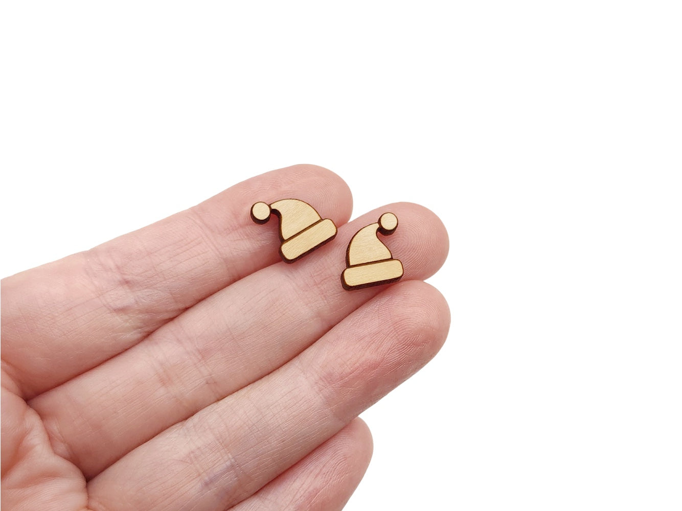 a hand holding a pair of wooden cabochon stud earring blanks cut and engraved to look like a Santa hat