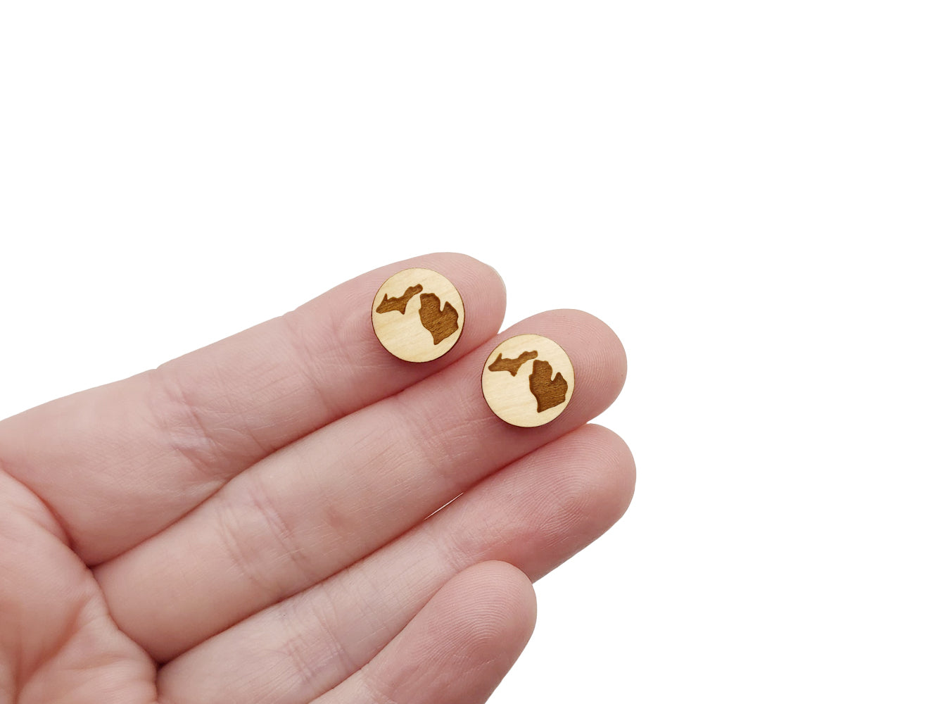 a hand holding a pair of round wooden cabochon earring blanks engraved with the State of Michigan