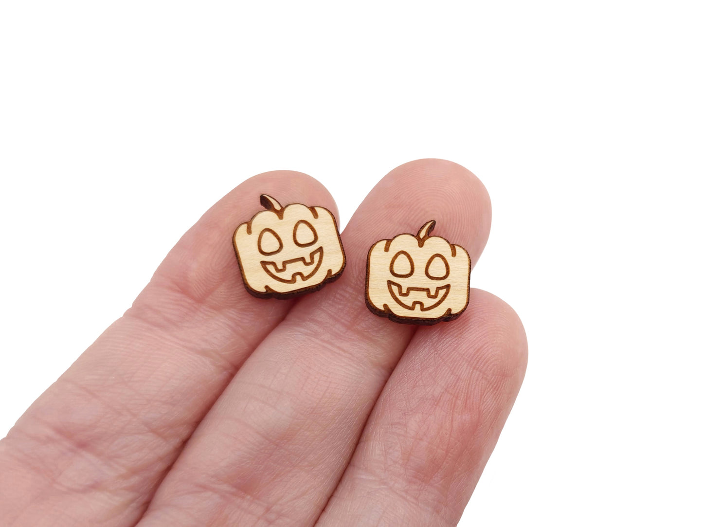 a hand holding a pair of wooden cabochon earring blanks cut and engraved to look like a happy jack-O-lantern