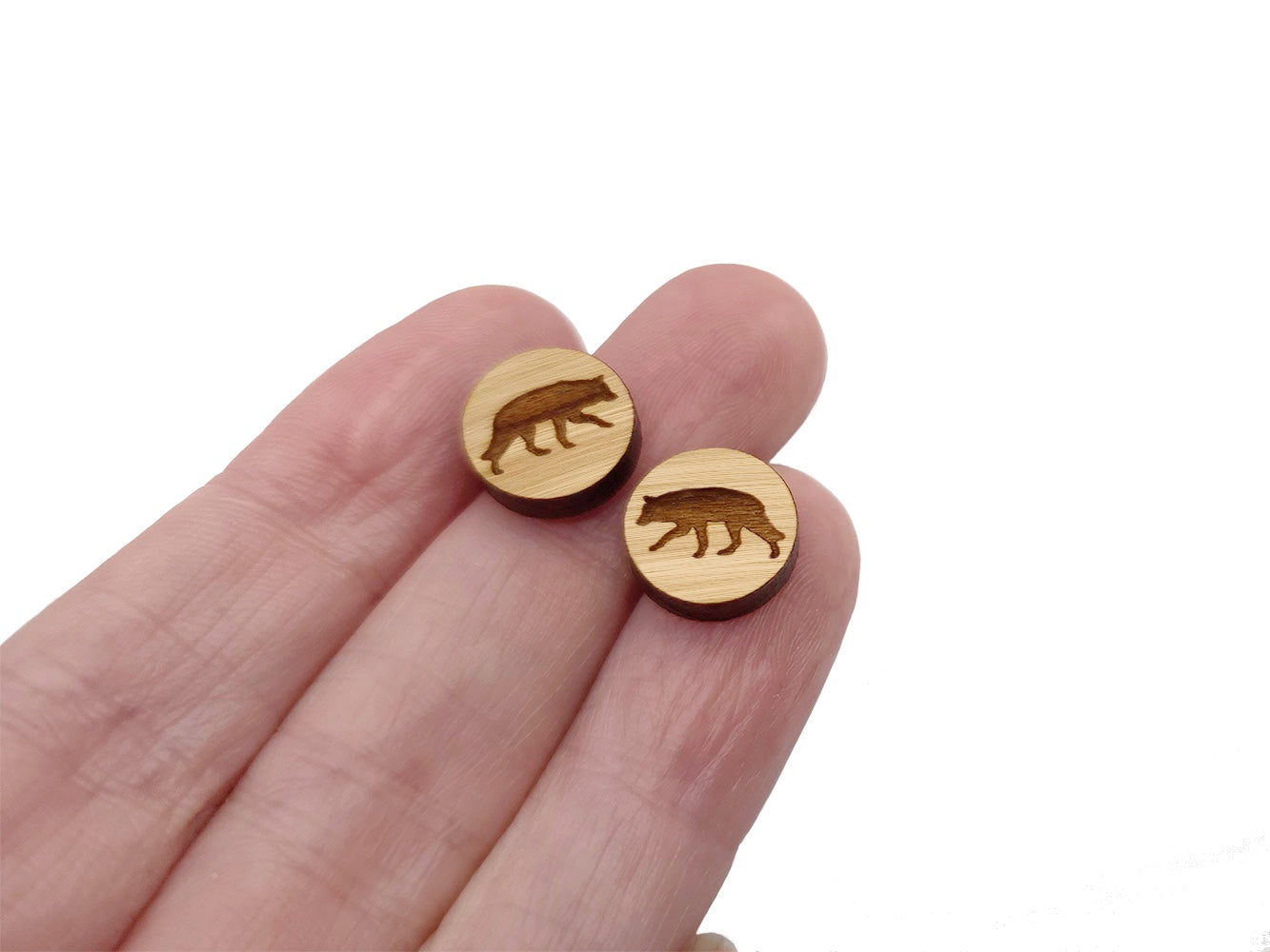 hand holding a pair of round wooden cabochon earring blanks engraved with a wolf silhouette design