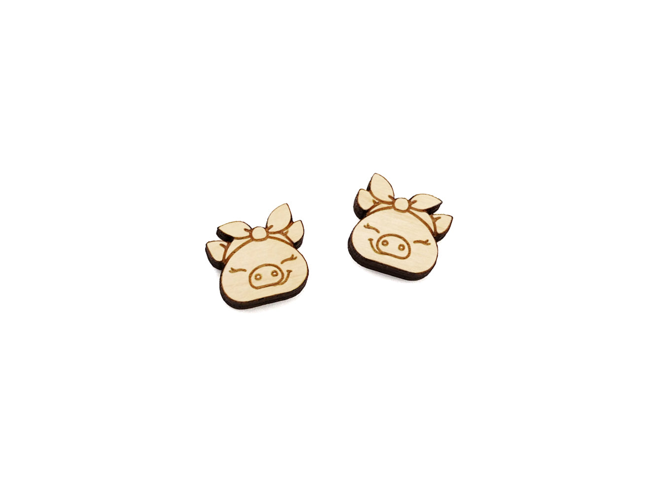 a pair of wooden cabochon stud earring blanks cut and engraved to look like pigs wearing a bandana