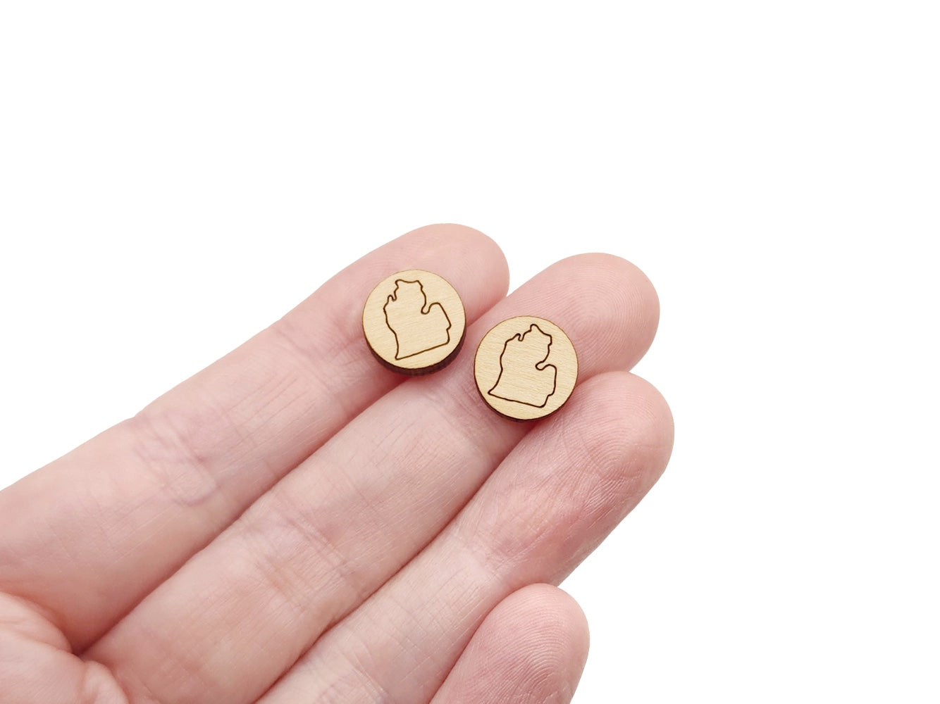 a hand holding a pair of round wooden cabochon earring blanks engraved with the outline of the Michigan Mitten