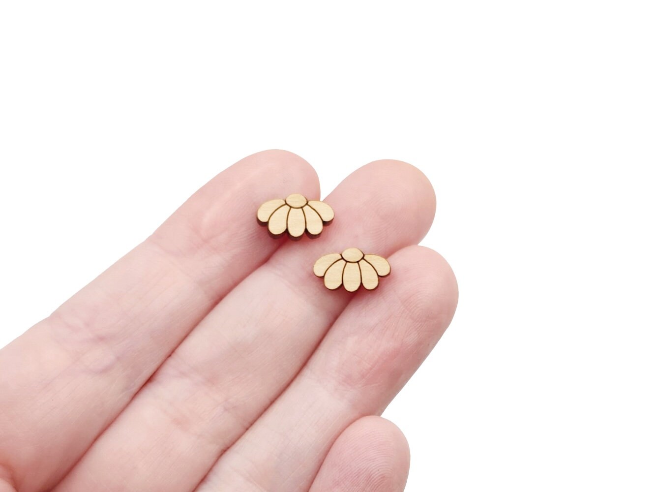 a hand holding a pair of wooden cabochon stud earring blanks cut and engraved to look like daisy flowers
