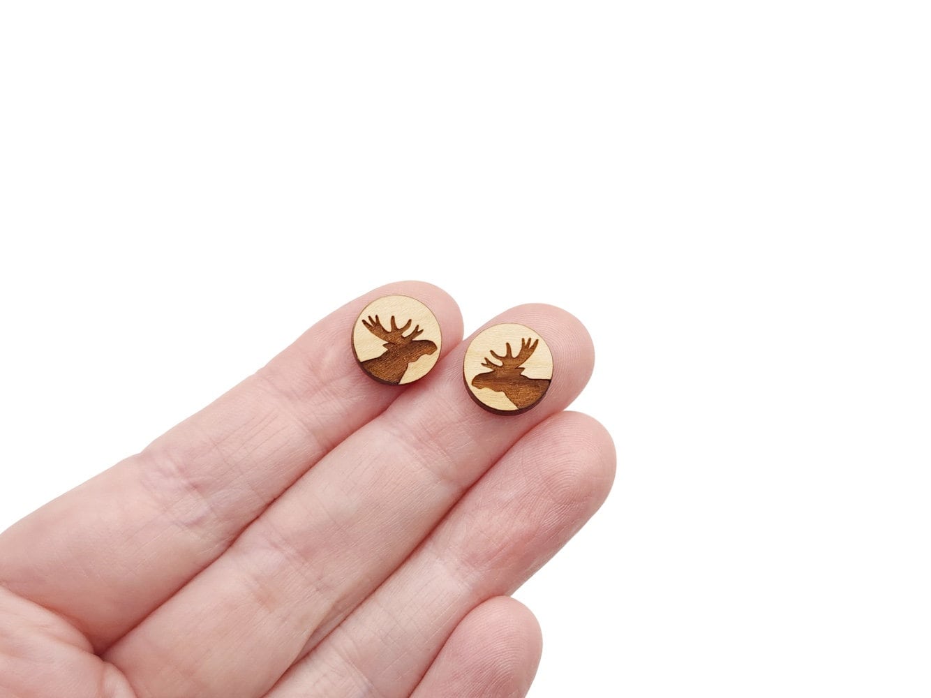 a hand holding a pair of round wooden cabochon stud earring blanks engraved with a moose silhouette