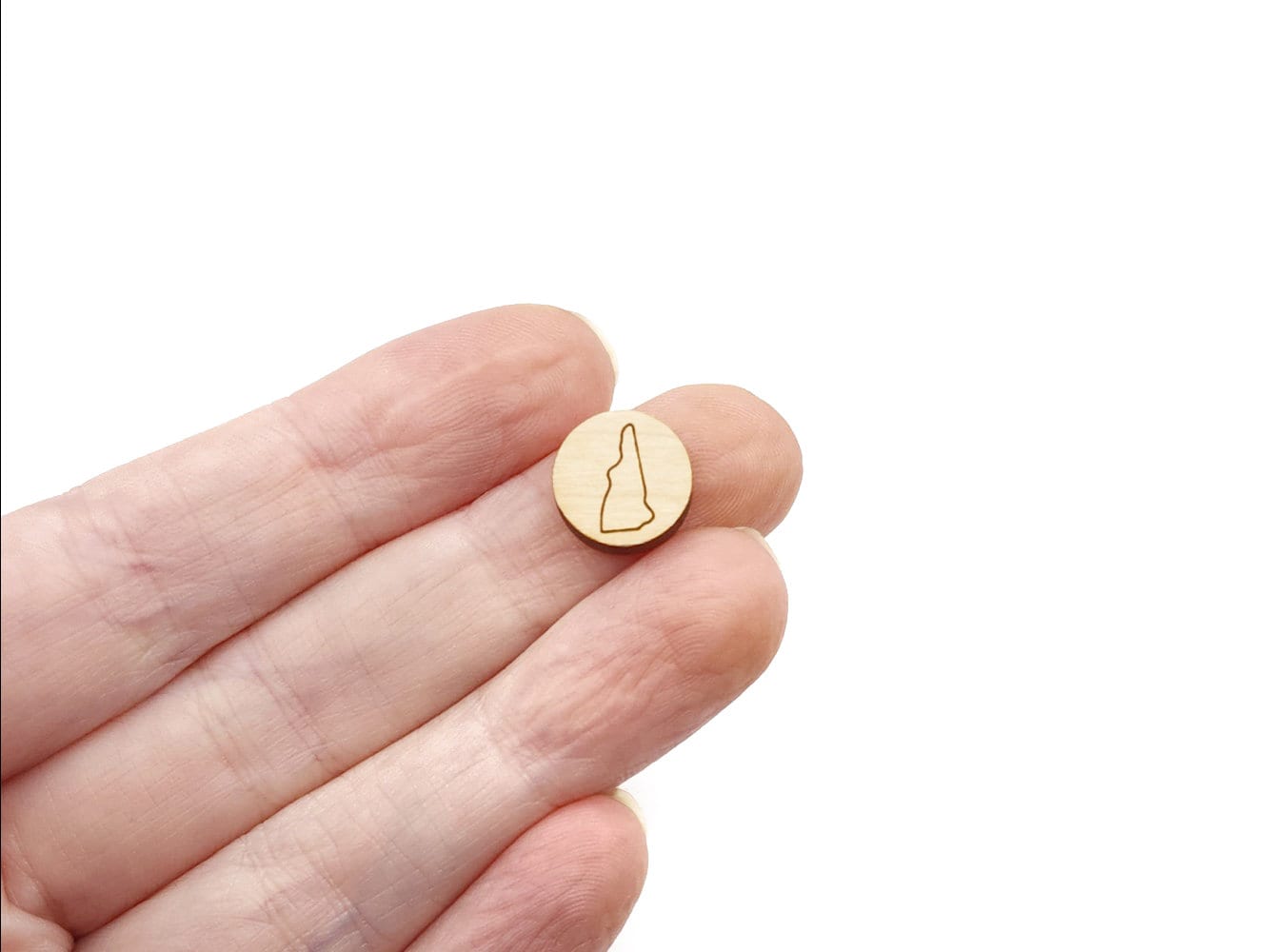a hand holding a round wooden cabochon earring blank engraved with an outline of New Hampshire