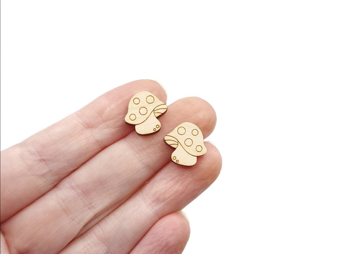 a hand holding a pair of wooden cabochon stud earring blanks cut and engraved to look like spotted mushrooms