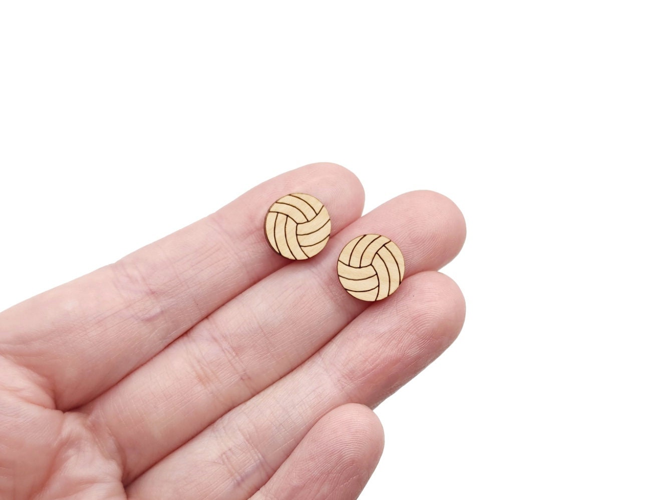 a hand holding a pair of wooden cabochon stud earring blanks cut and engraved to look like volleyballs