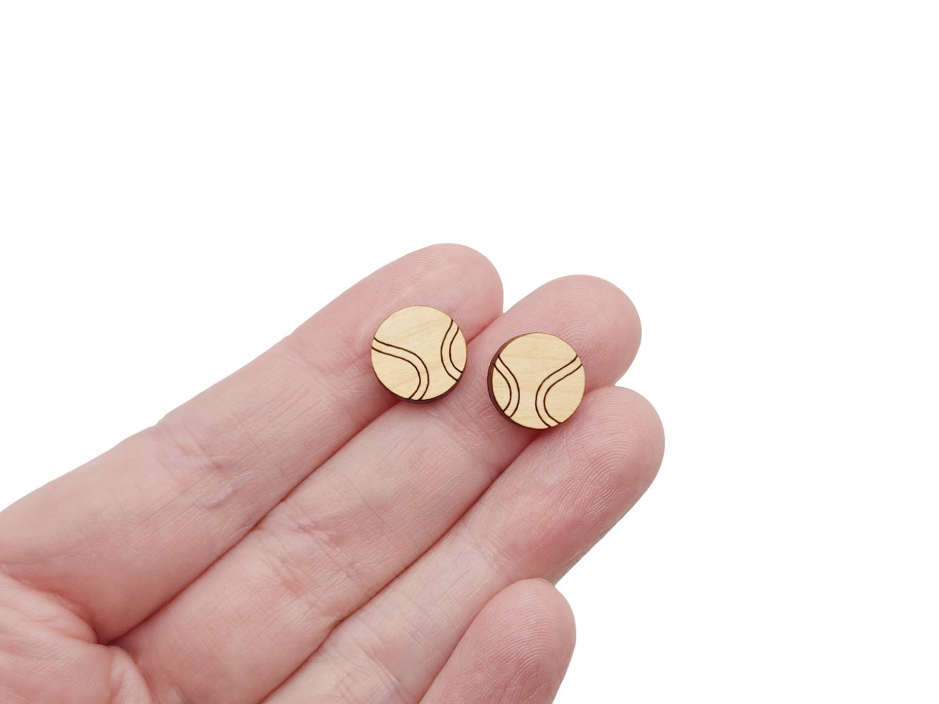 a hand holding a pair of wooden cabochon stud earring blanks cut and engraved to look like tennis balls