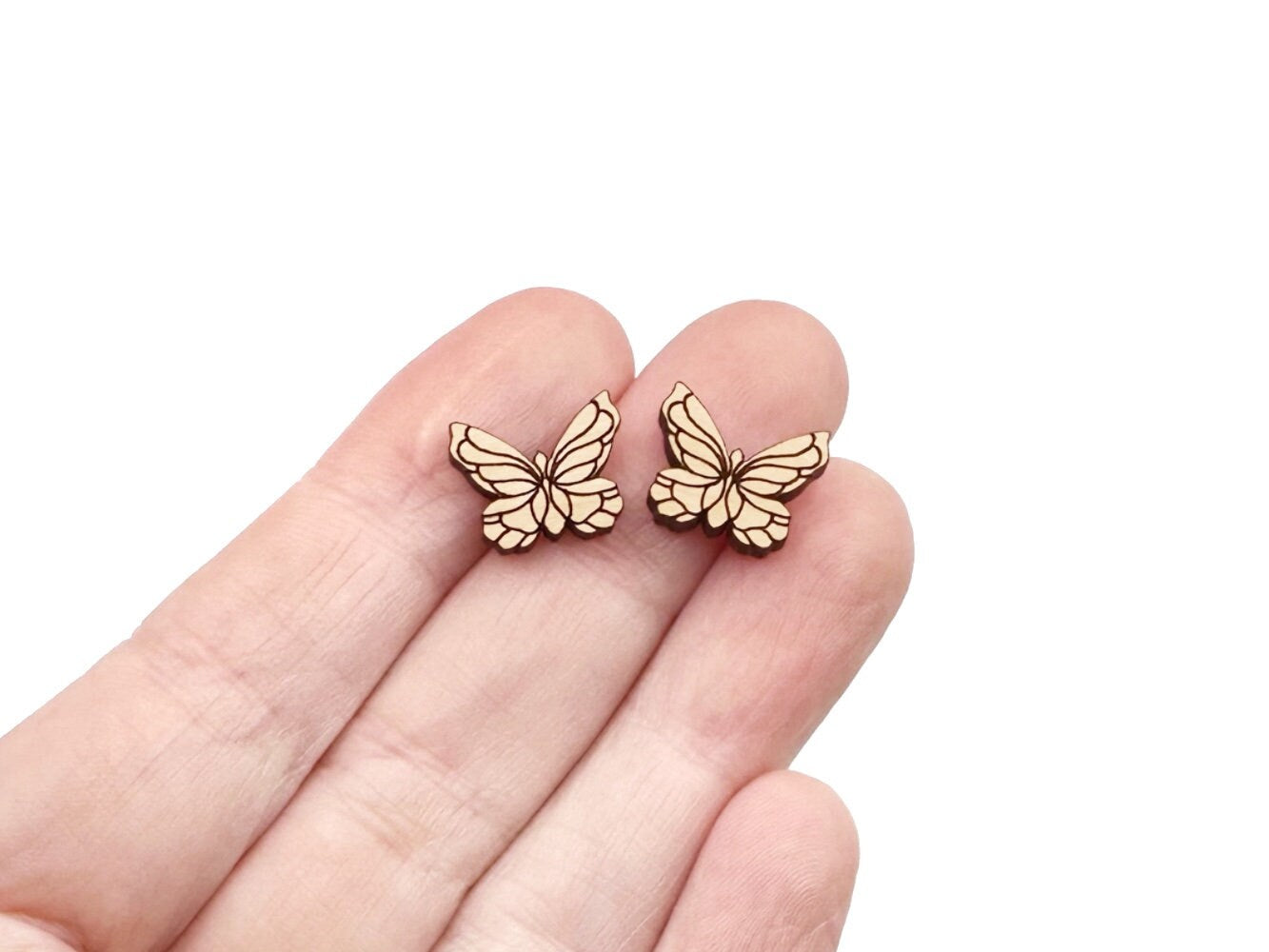 a hand holding a pair of wooden cabochon stud earring blanks cut and engraved to look like butterflies