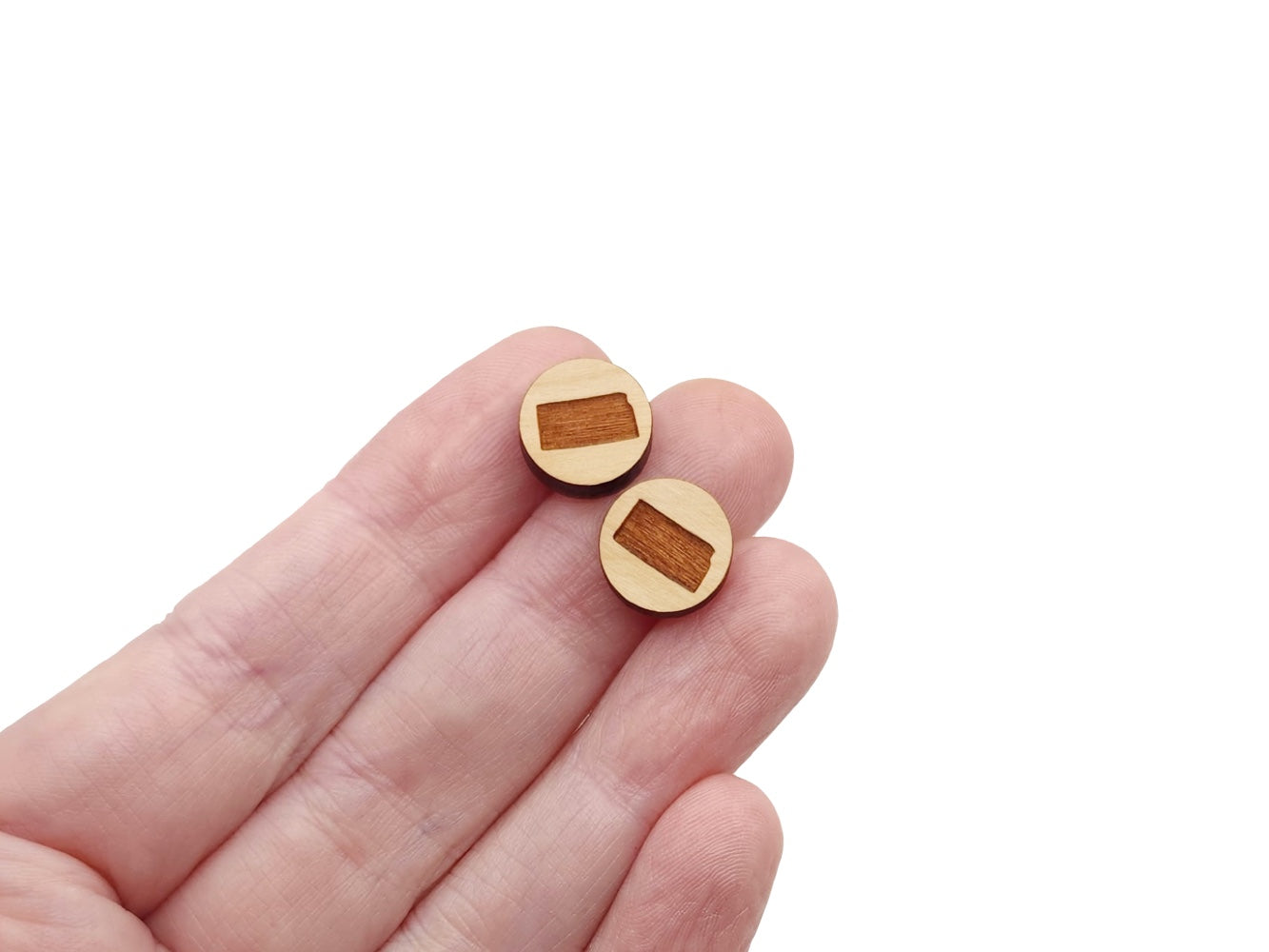 a hand holding a pair of round wooden cabochon earring blanks engraved with the state of Kansas