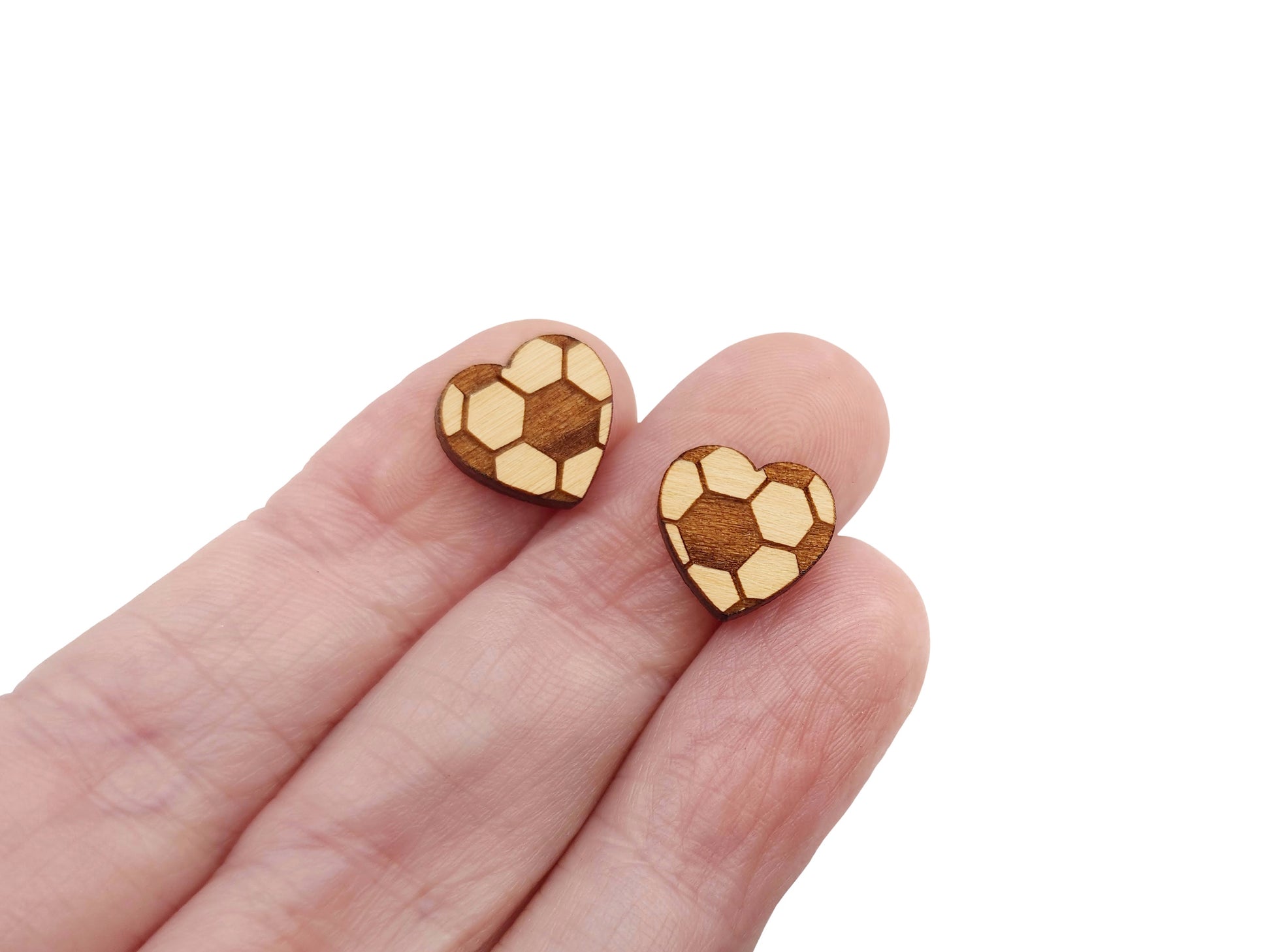 a hand holding a pair of wooden cabochon earring blanks cut and engraved to look like a heart-shaped soccer ball