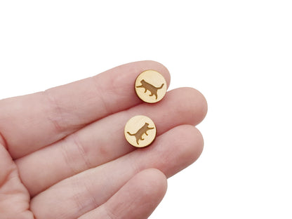 a hand holding a pair of round wooden cabochon earring blanks engraved with a cat silhouette