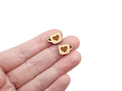 a hand holding a pair of wooden cabochon stud earring blanks cut and engraved to look like a mug with a heart