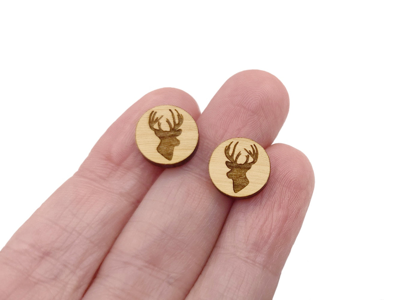 a hand holding a pair of earrings with a deer head on it