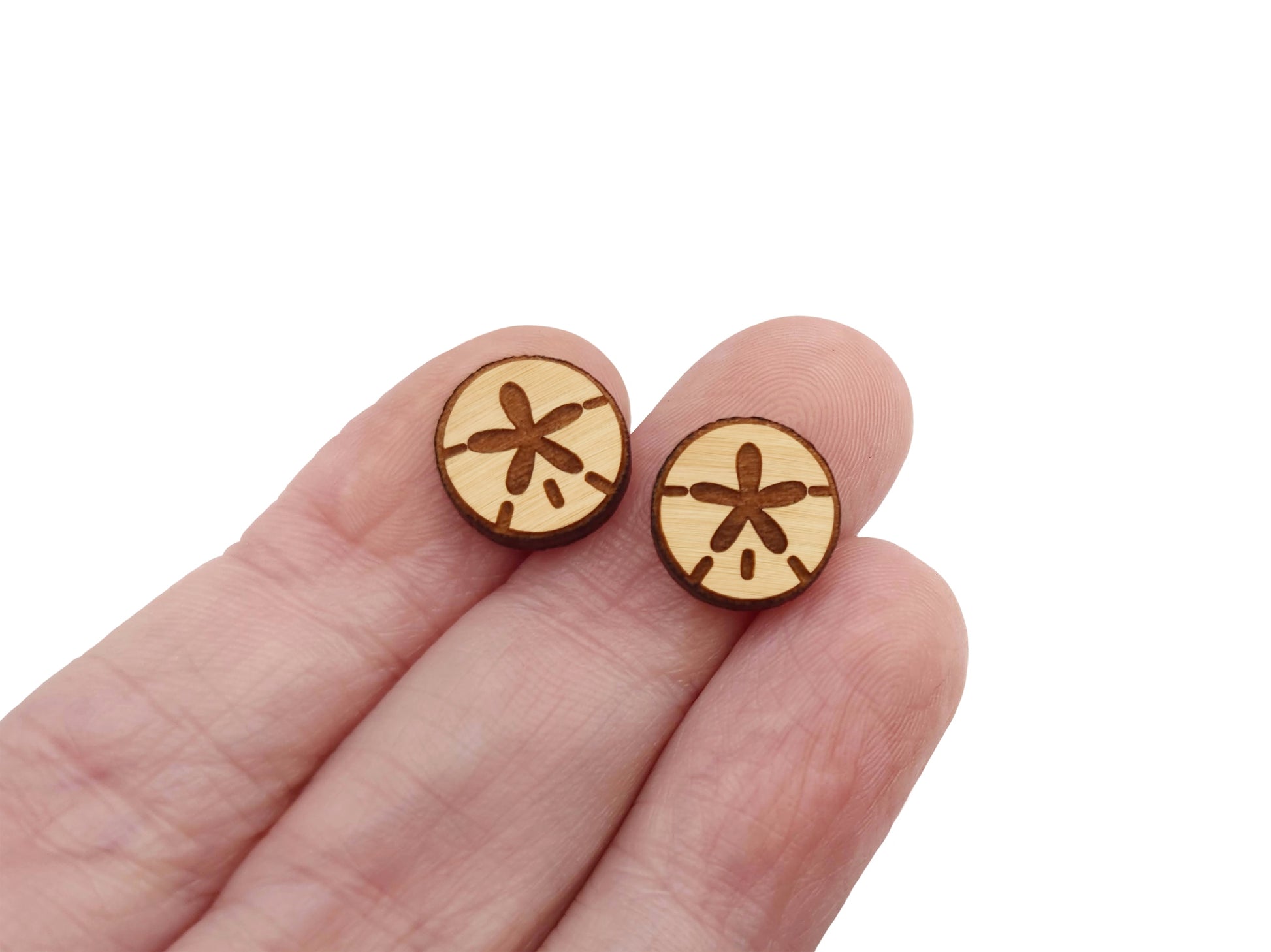 a hand holding a pair of wooden cabochon stud earring blanks cut and engraved to look like a sand dollar