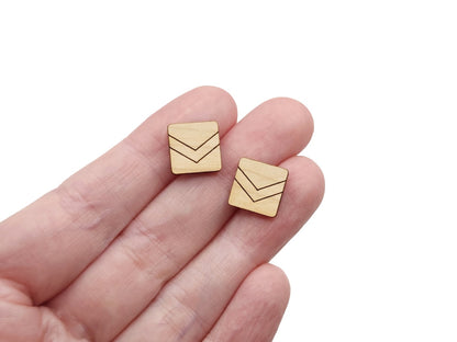 a hand holding a pair of wooden cabochon stud earring blanks cut in a square shape and engraved with a chevron