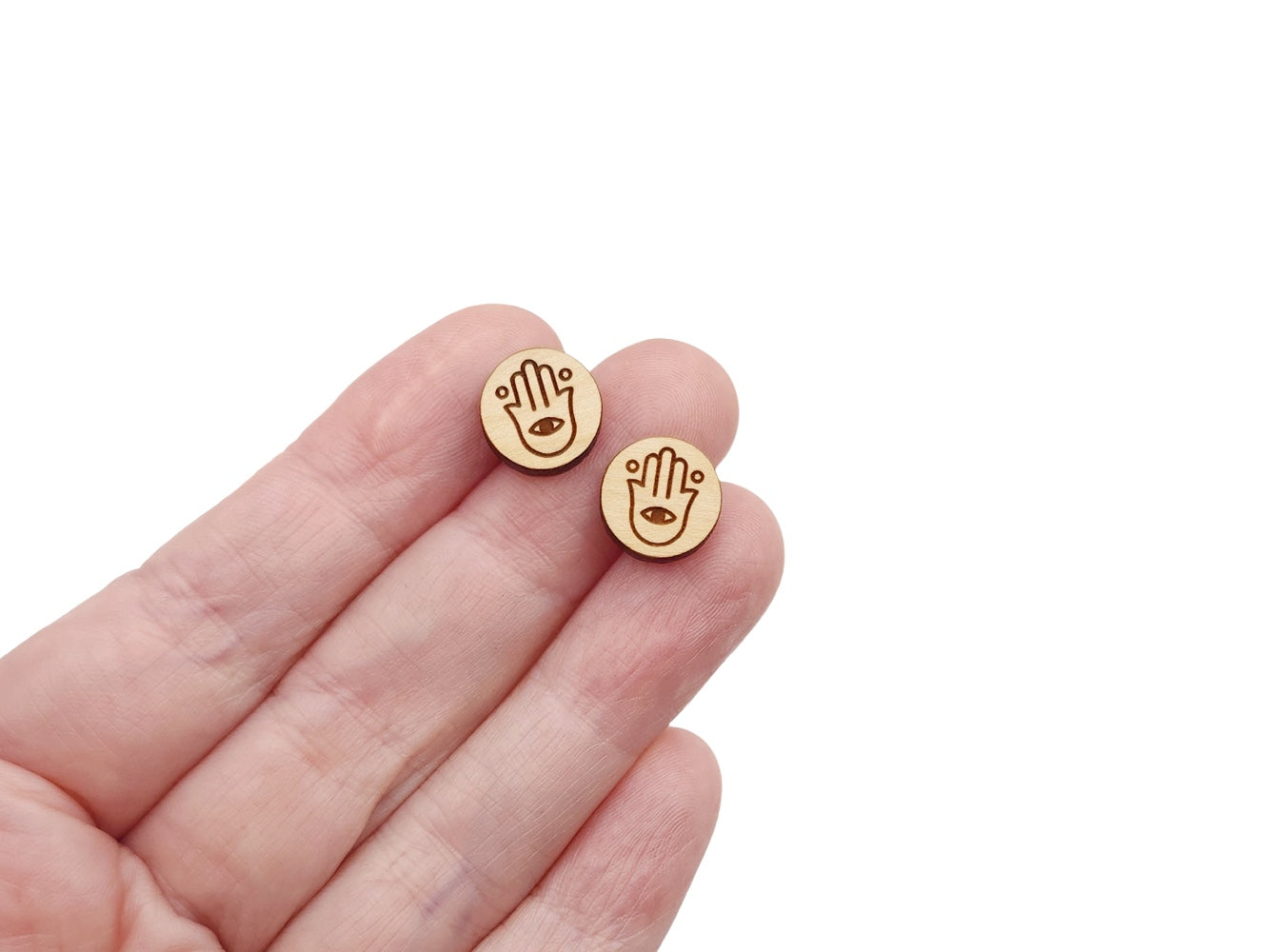 a hand holding a pair of round wooden cabochon earring blanks engraved with a pair of hamsa design