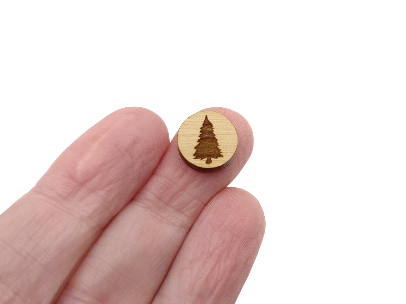 a hand holding a round wooden cabochon earring blank engraved with a pine tree silhouette