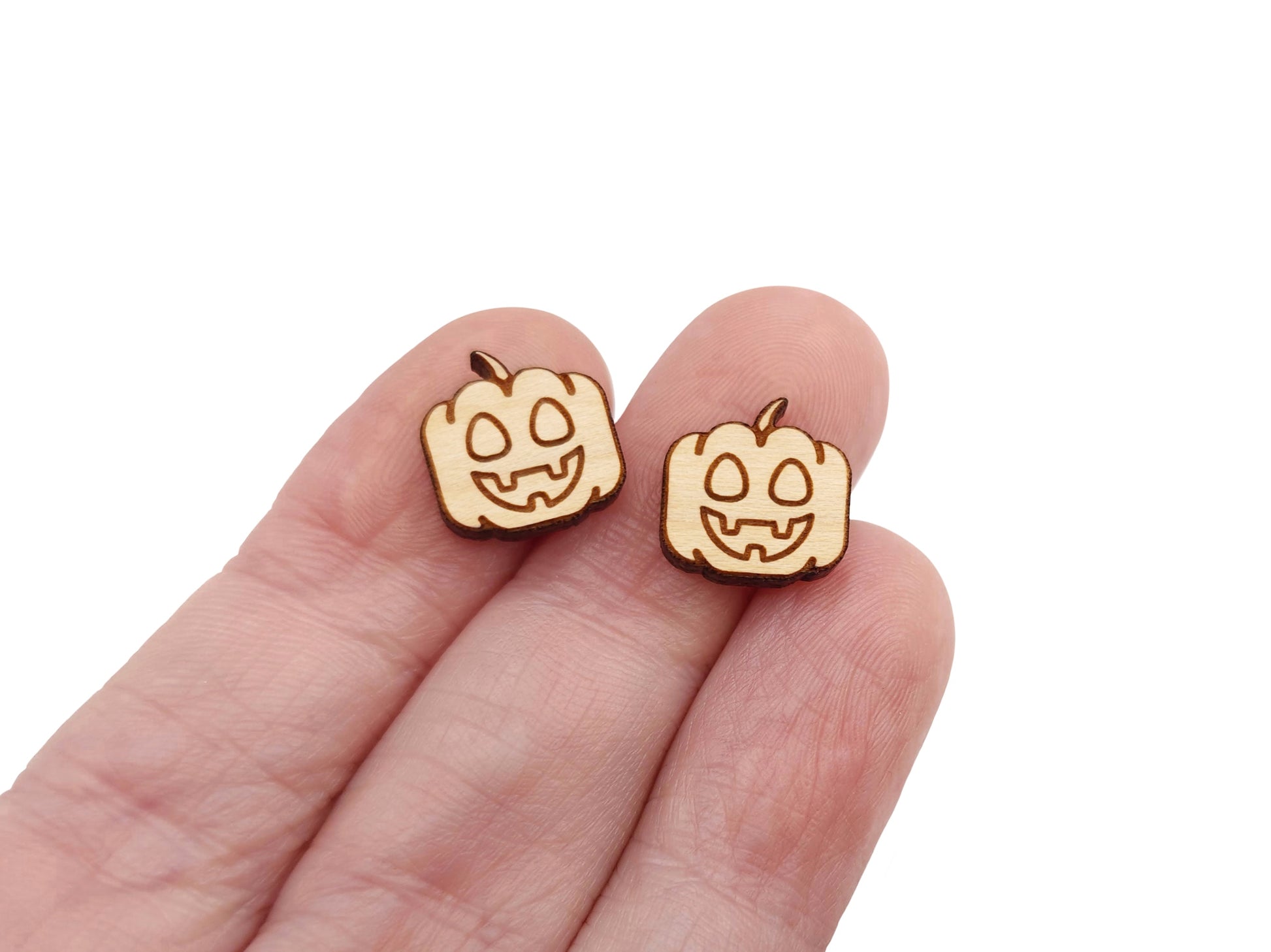 a hand holding a pair of wooden cabochon earring blanks cut and engraved to look like a happy jack-O-lantern