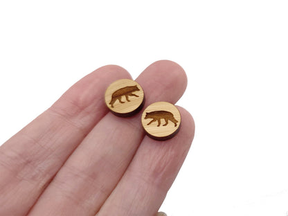 hand holding a pair of round wooden cabochon earring blanks engraved with a wolf silhouette design