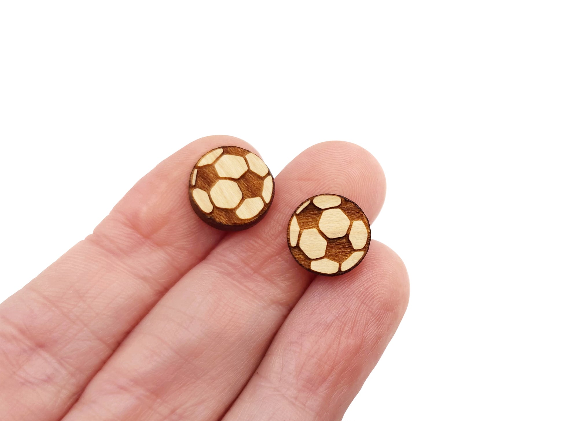 a hand holding a pair of wooden cabochon earring blanks cut and engraved to look like a soccer ball