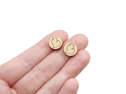 a hand holding a pair of round wooden cabochon earring blanks engraved with the outline of the Michigan Mitten