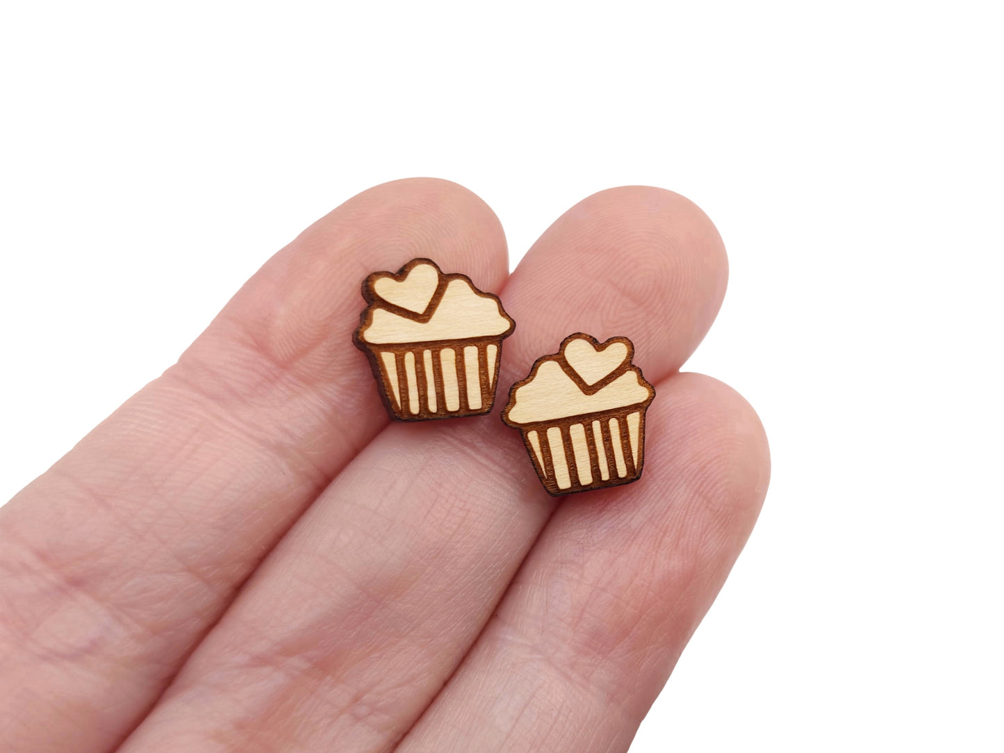 a hand holding a pair of wooden cabochon stud earring blanks cut and engraved to look like a cupcake