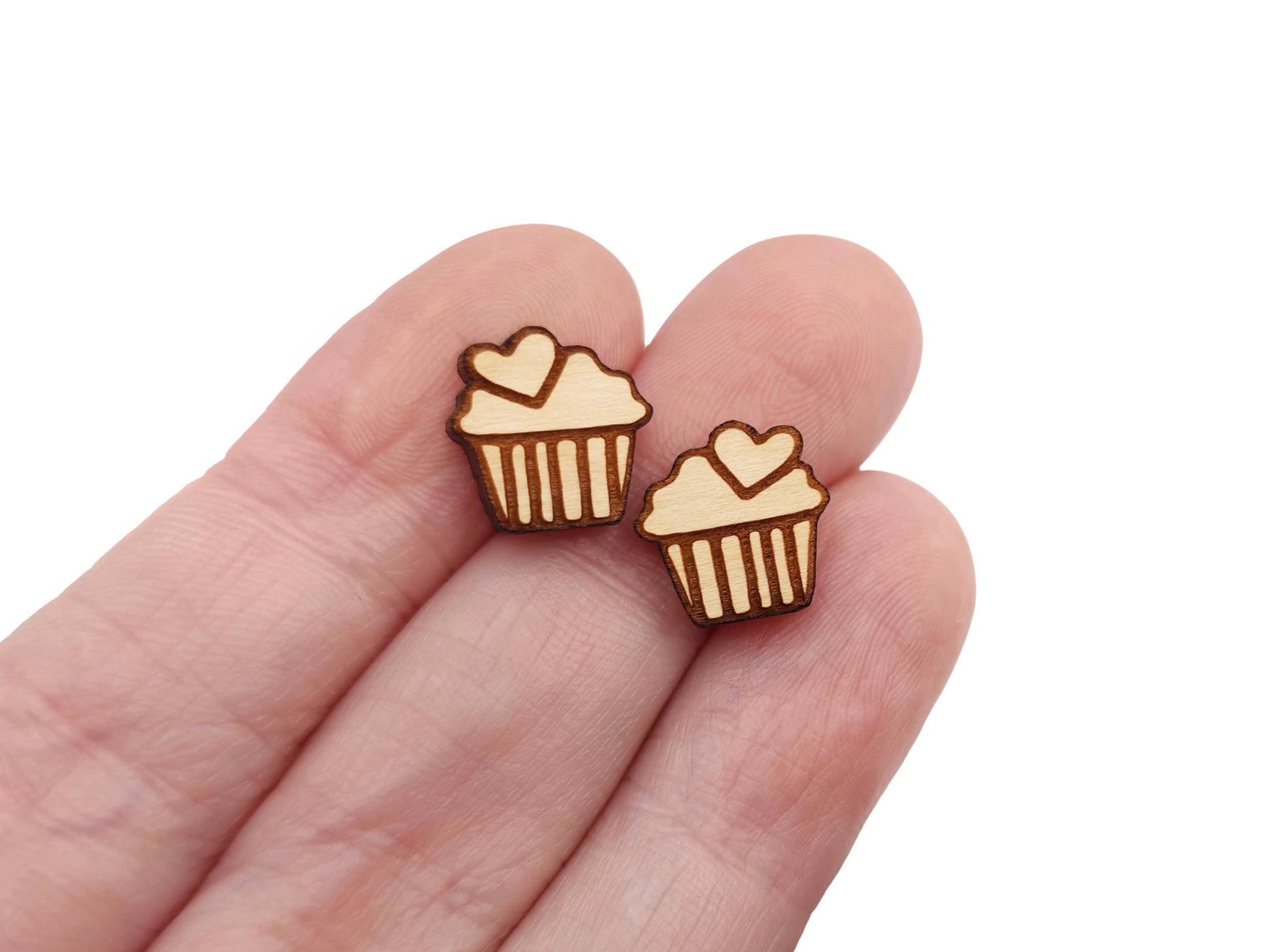 a hand holding a pair of wooden cabochon stud earring blanks cut and engraved to look like a cupcake