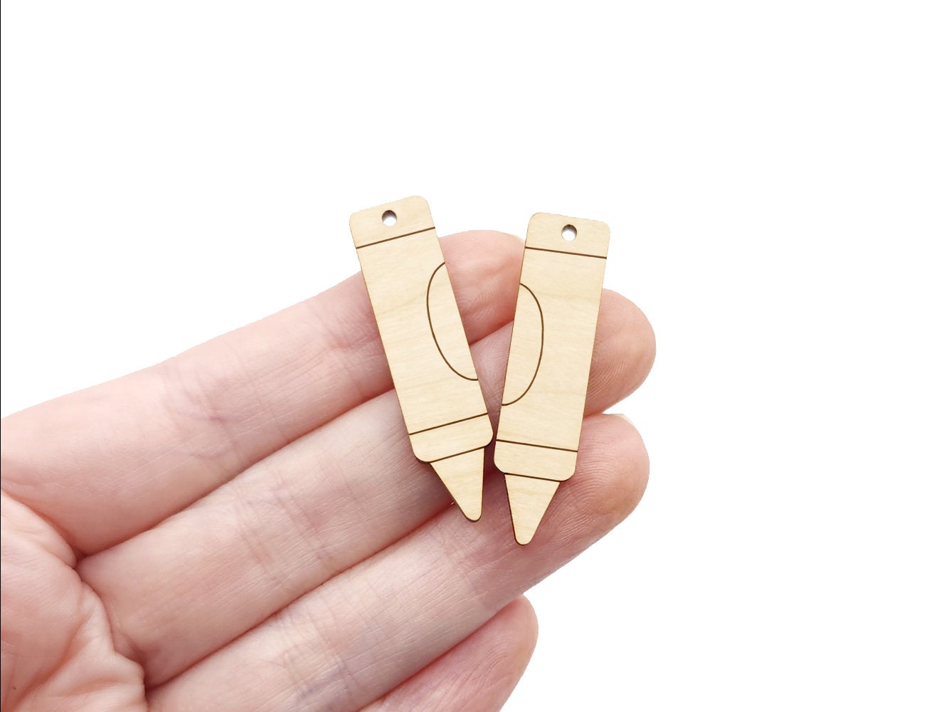 a hand holding a pair of wooden earring blanks cut and engraved to look like a crayon