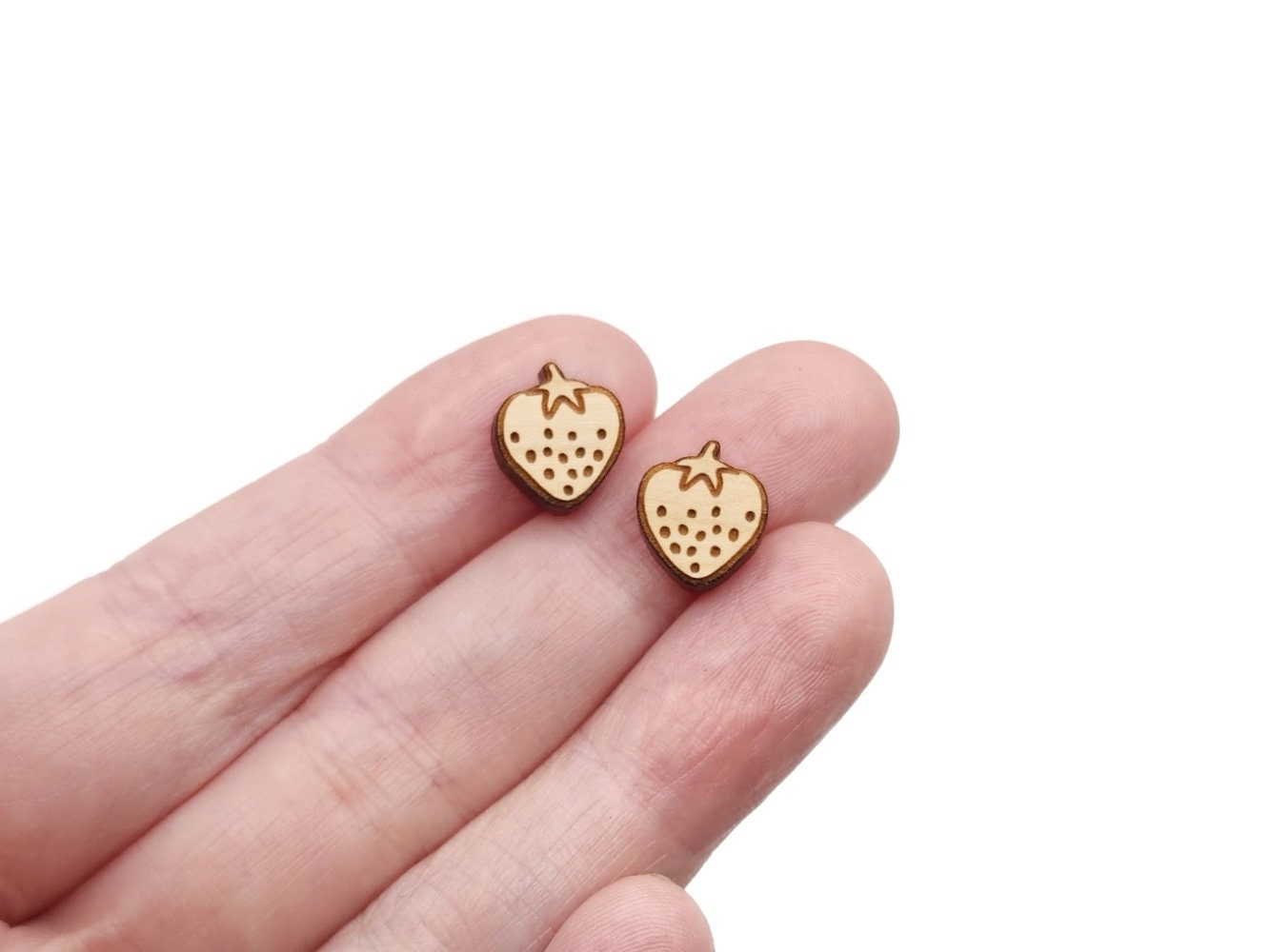 hand holding a pair of wooden cabochon earring blanks cut and engraved to look like a strawberry.