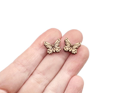 a hand holding a pair of wooden cabochon stud earring blanks cut and engraved to look like butterflies