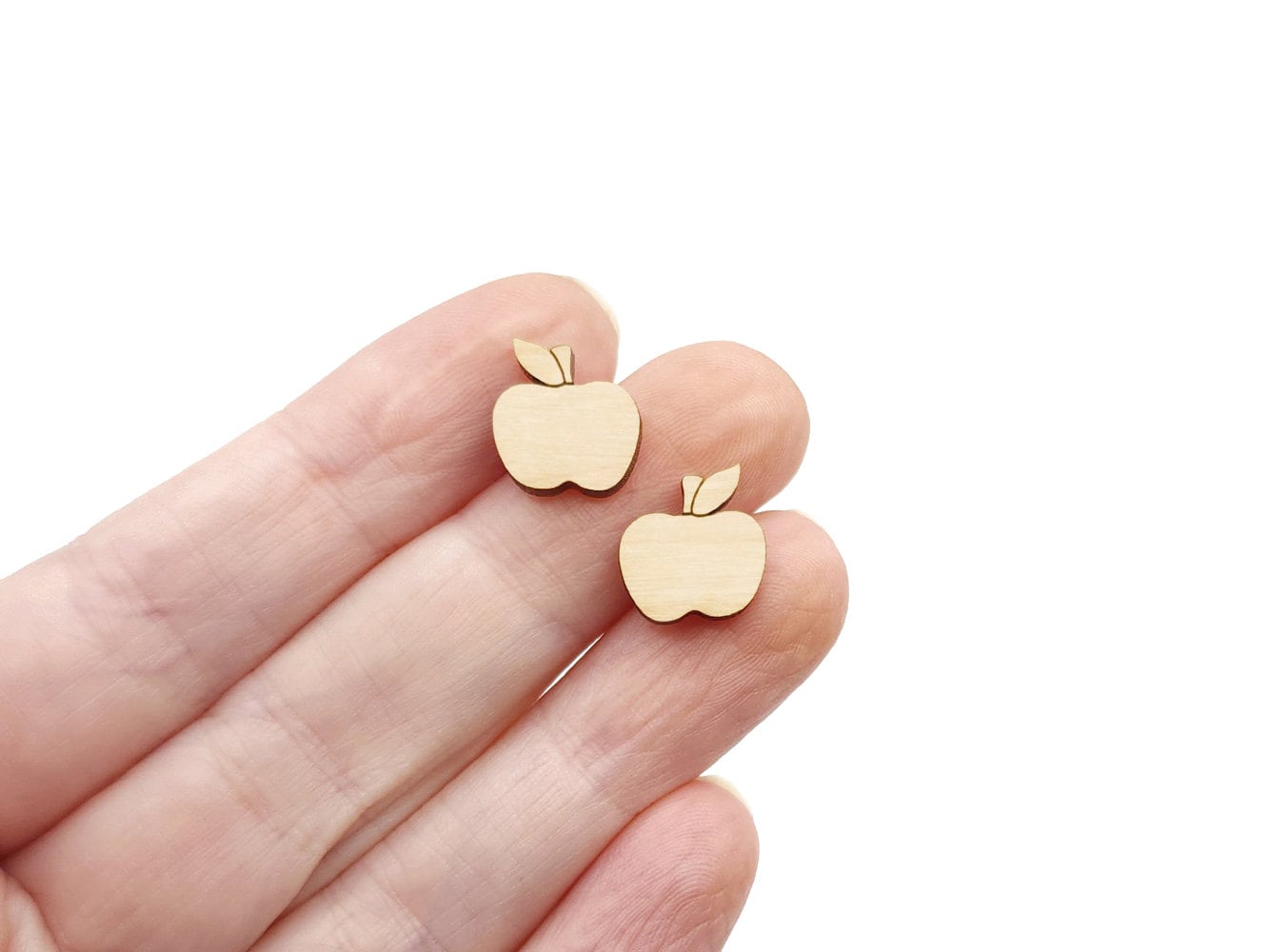 a hand holding a pair of wooden cabochon stud earring blanks cut and engraved to look like an apple