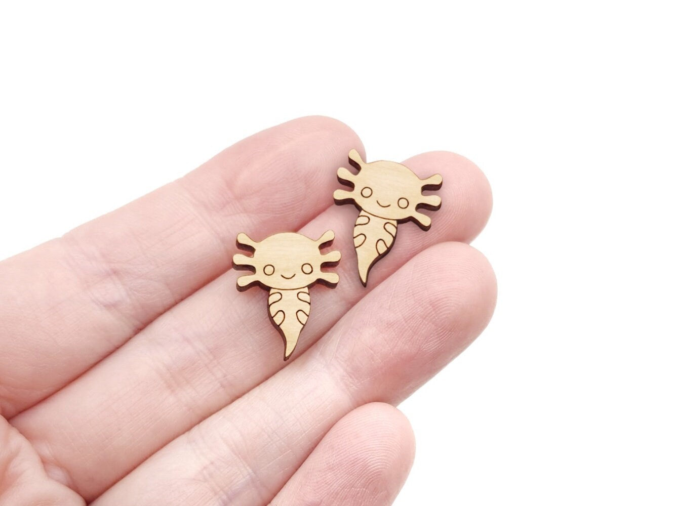 a hand holding a pair of wooden cabochon stud earring blanks cut and engraved to look like axolotls